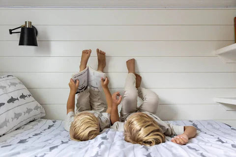 
      Two boys laying on a bed with zipper bedding reading a book together.
    