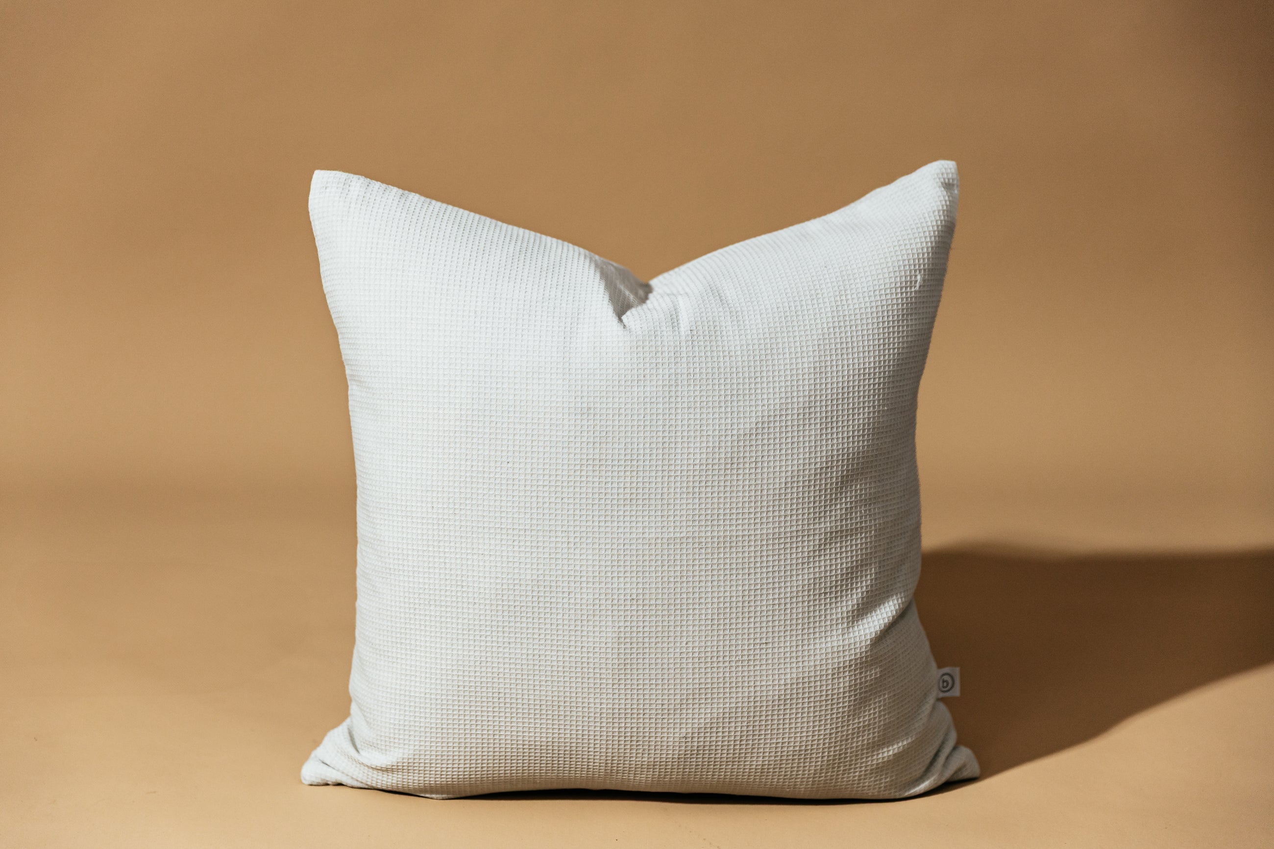 A light gray pillow on a brown backdrop.