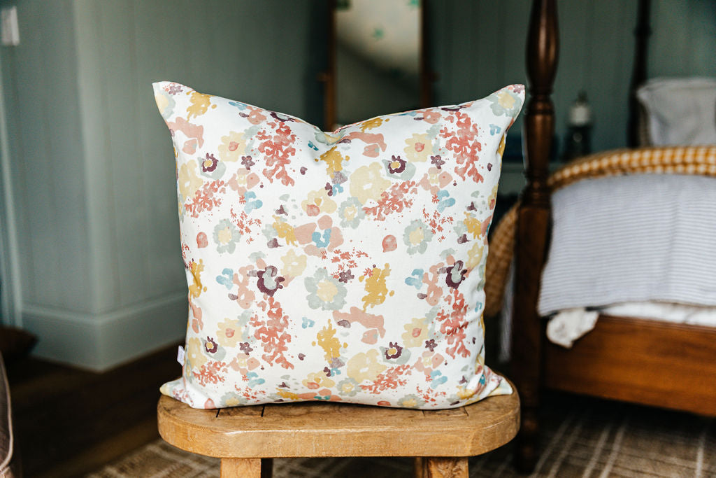 A floral throw pillow sitting on a wood bench in a bedroom.