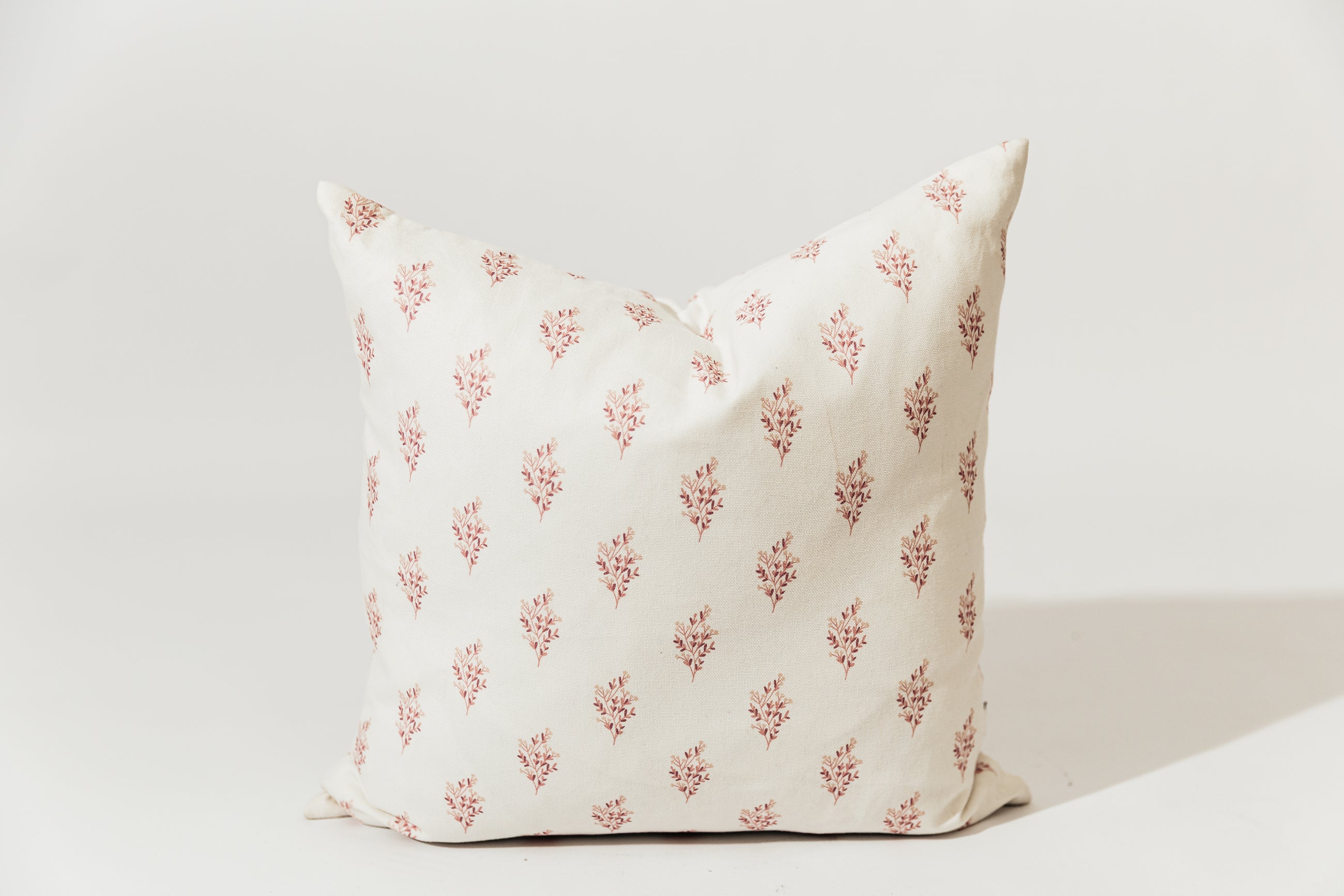 A pink floral pillow on a white backdrop.