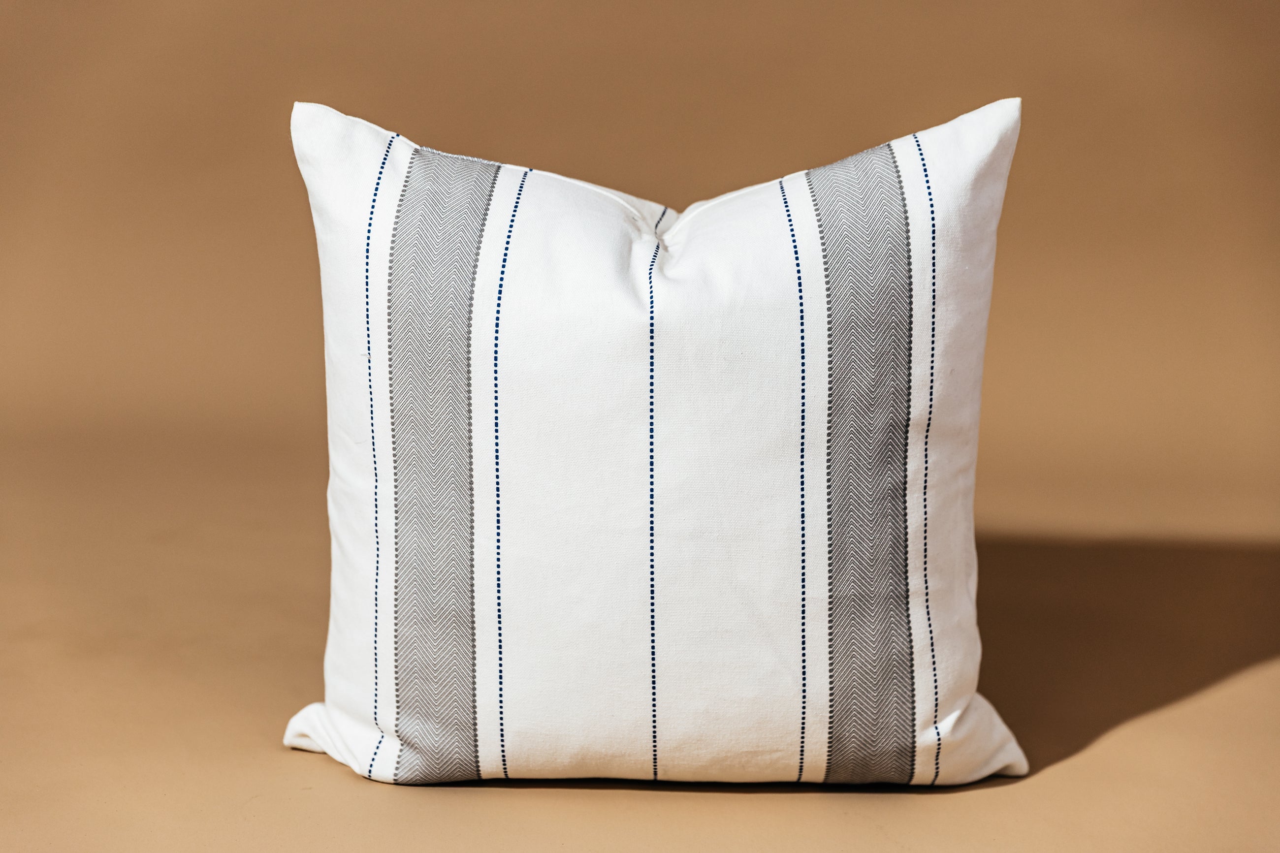 A white, gray, and navy stripe pillow on a brown backdrop.