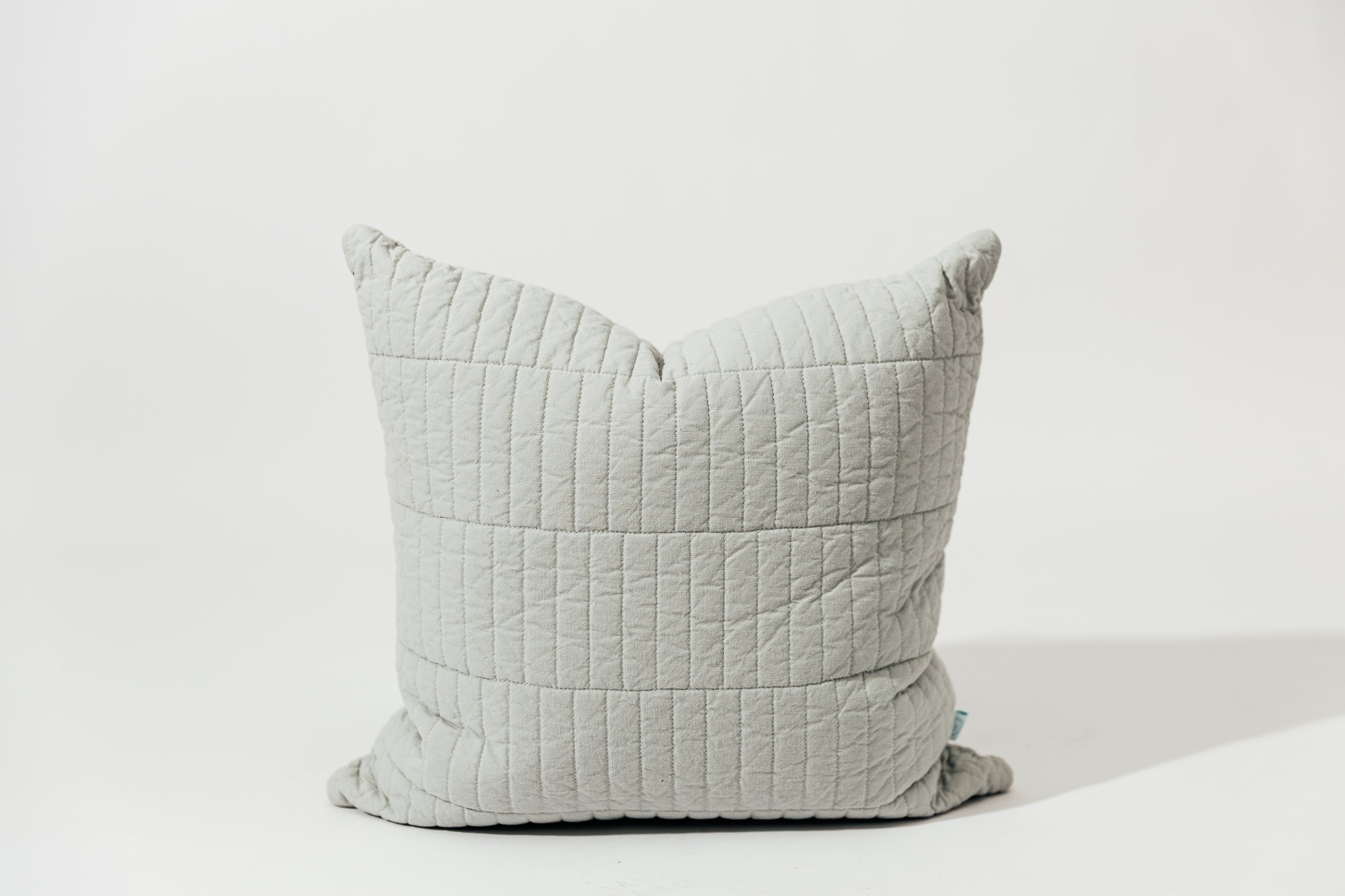 A blue pillow cover with piano tile quilted detail on a white backdrop.