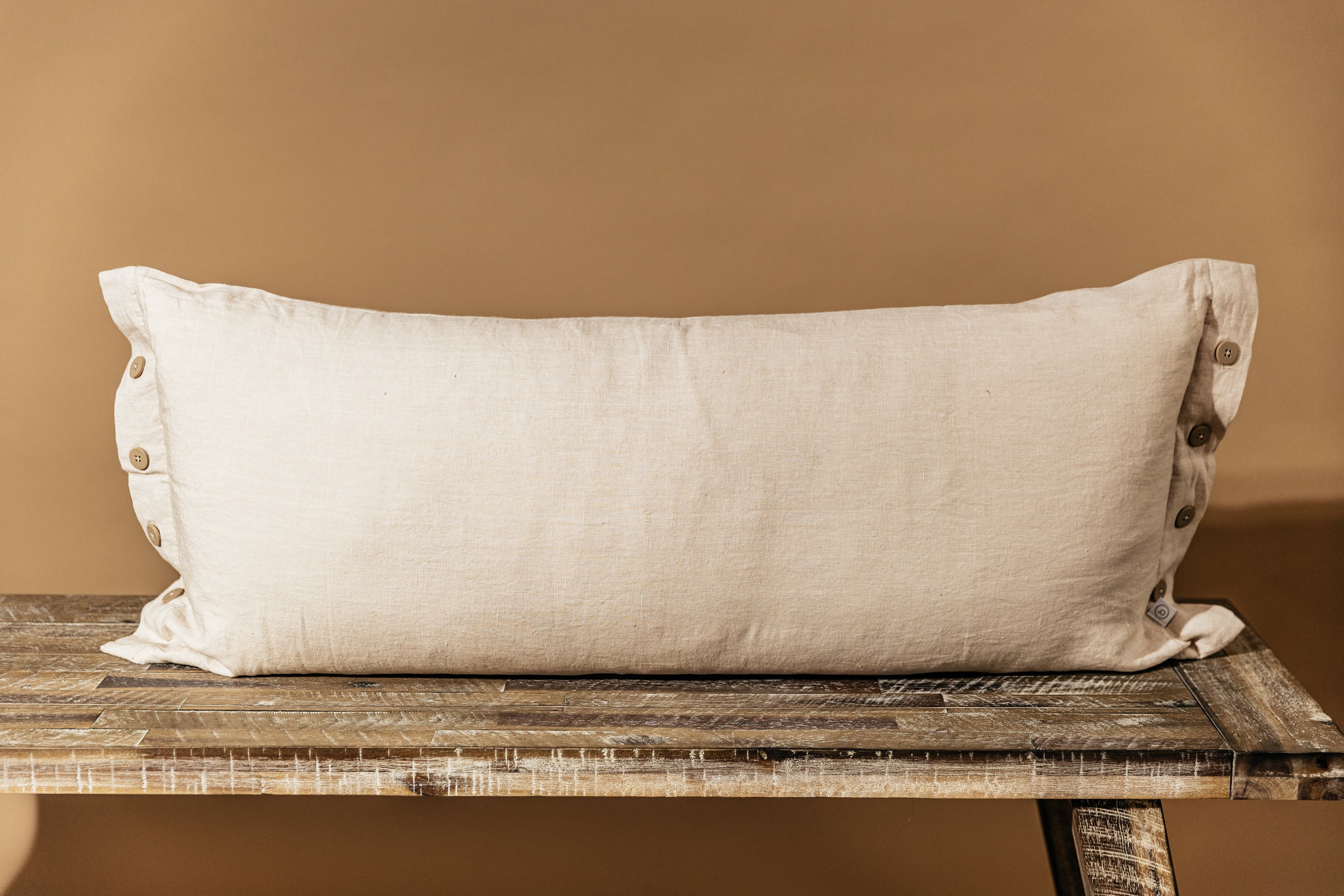 A linen lumbar pillow on a wood bench in front of a brown backdrop.