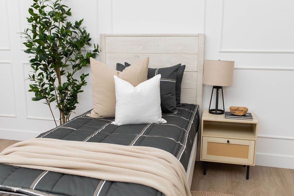A twin bed made with charcoal, white, and tan plaid zipper bedding and neutral and white pillows and blanket.
