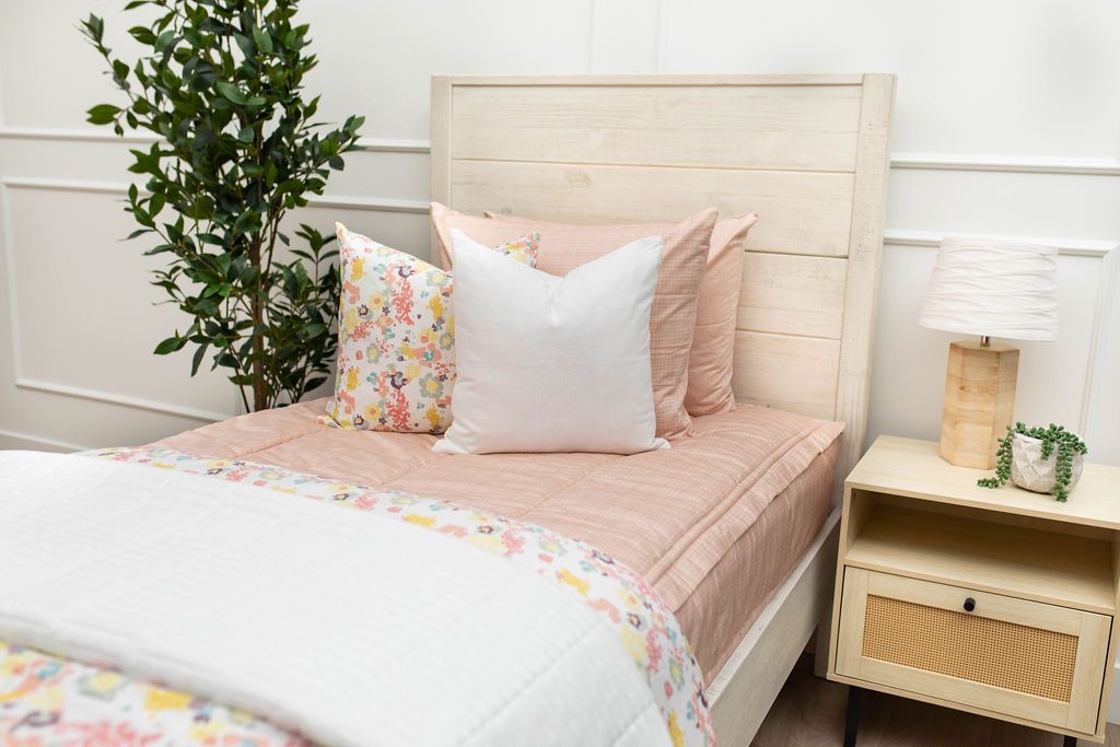 A twin bed made with light pink zipper bedding and white and multicolored floral pillows and blankets.