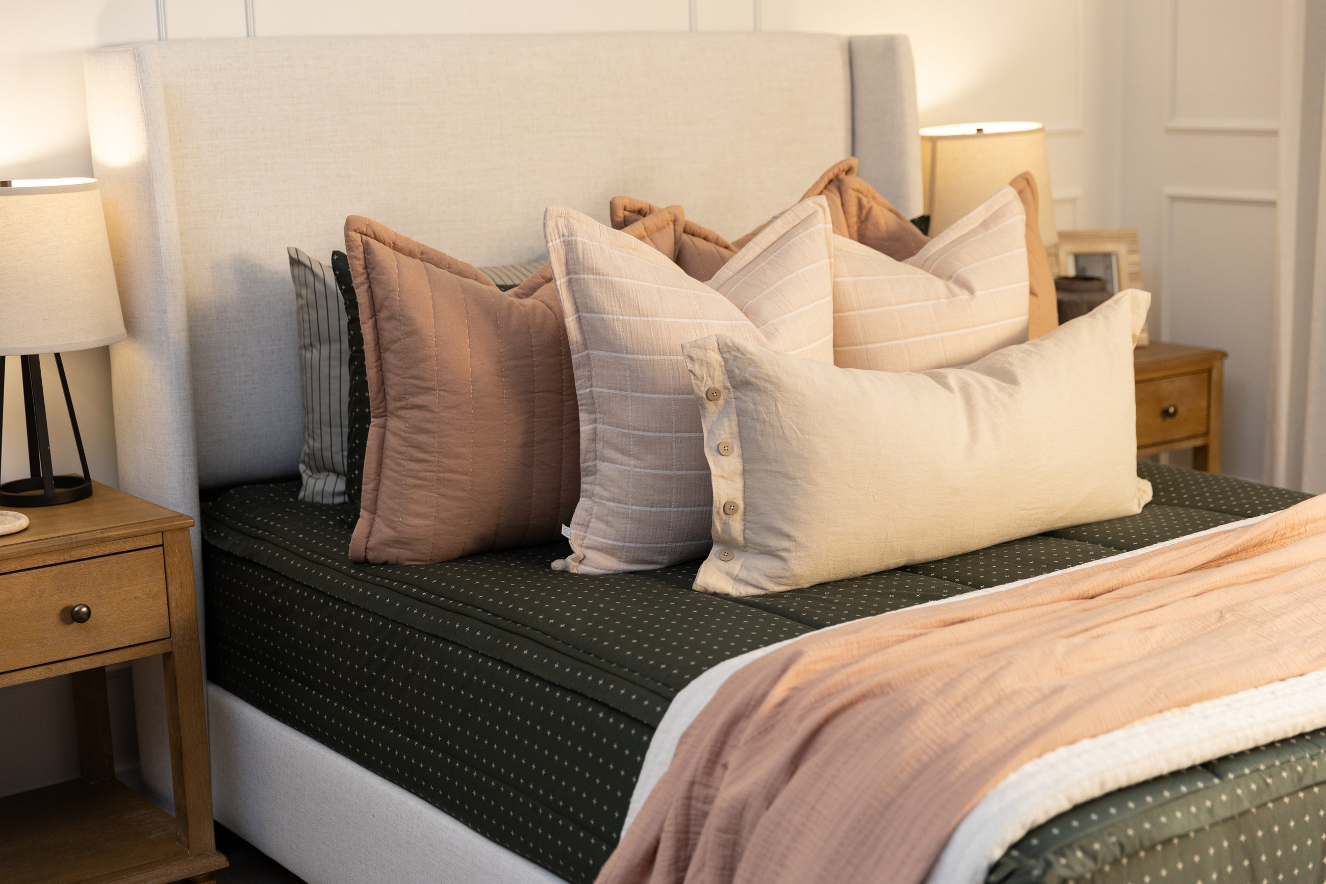 A dark green beddys with an assortment of pink and terracotta bedding accessories, including a lumbar linen pillow.
