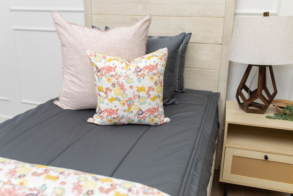 A bed made with gray zipper bedding and pink and floral throw pillows.