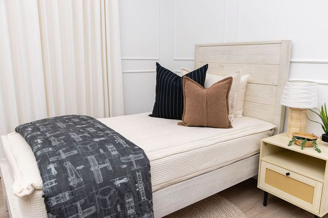 A twin bed made with cream waffle textured zipper bedding and an assortment of neutral throw pillows and an airplane pattern black blanket.