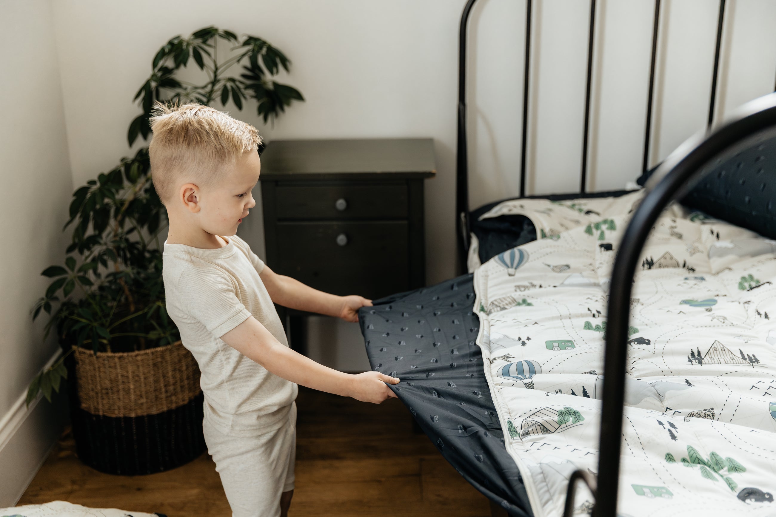 A young boy pulling the comfort panel out on a bed made with outdoor-themed zipper bedding.