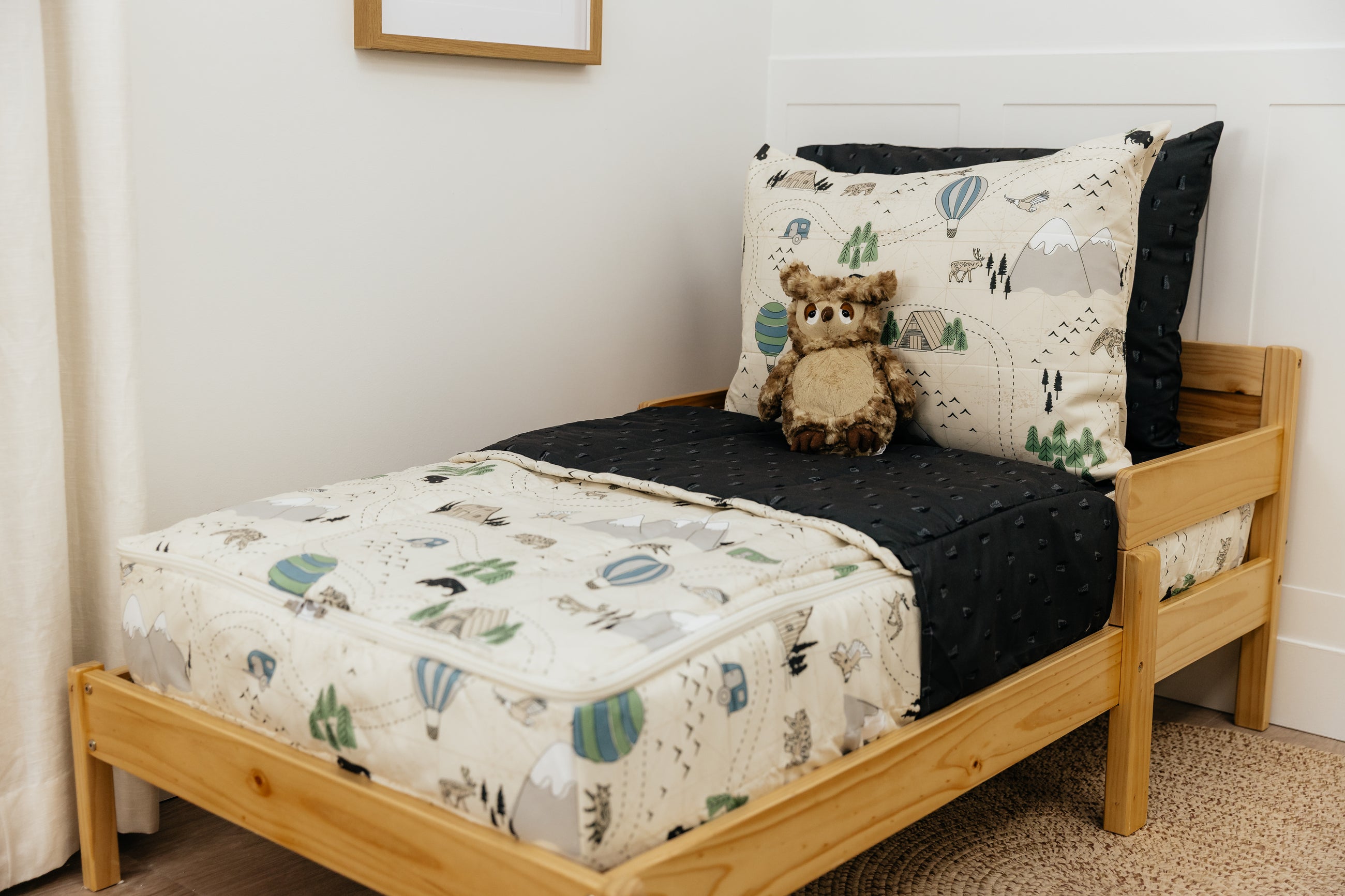A toddler bed made with outdoor themed zipper bedding, a stuffed owl propped up against the pillows.