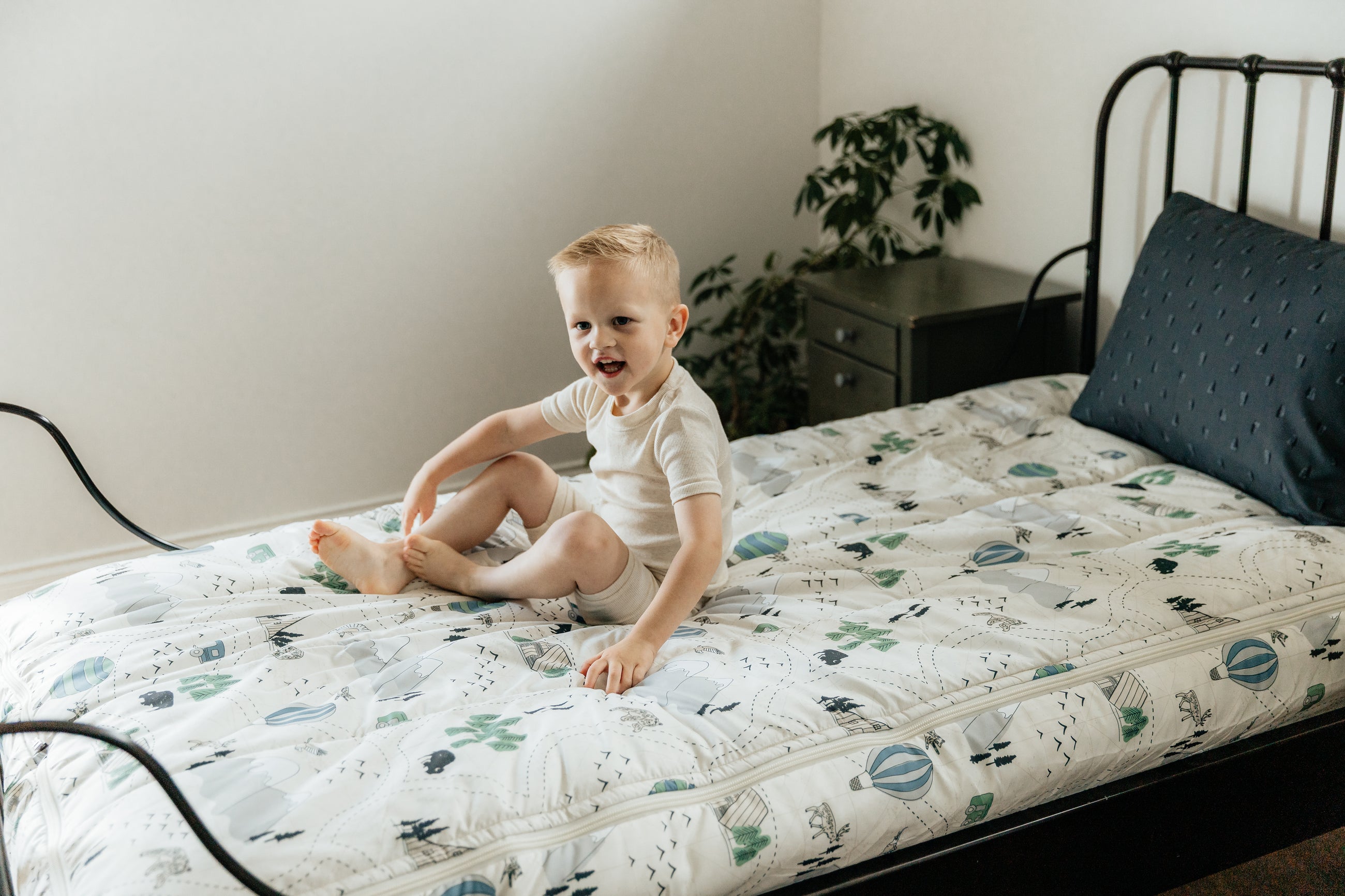 A young boy sitting on a twin bed made with outdoor themed zipper bedding.