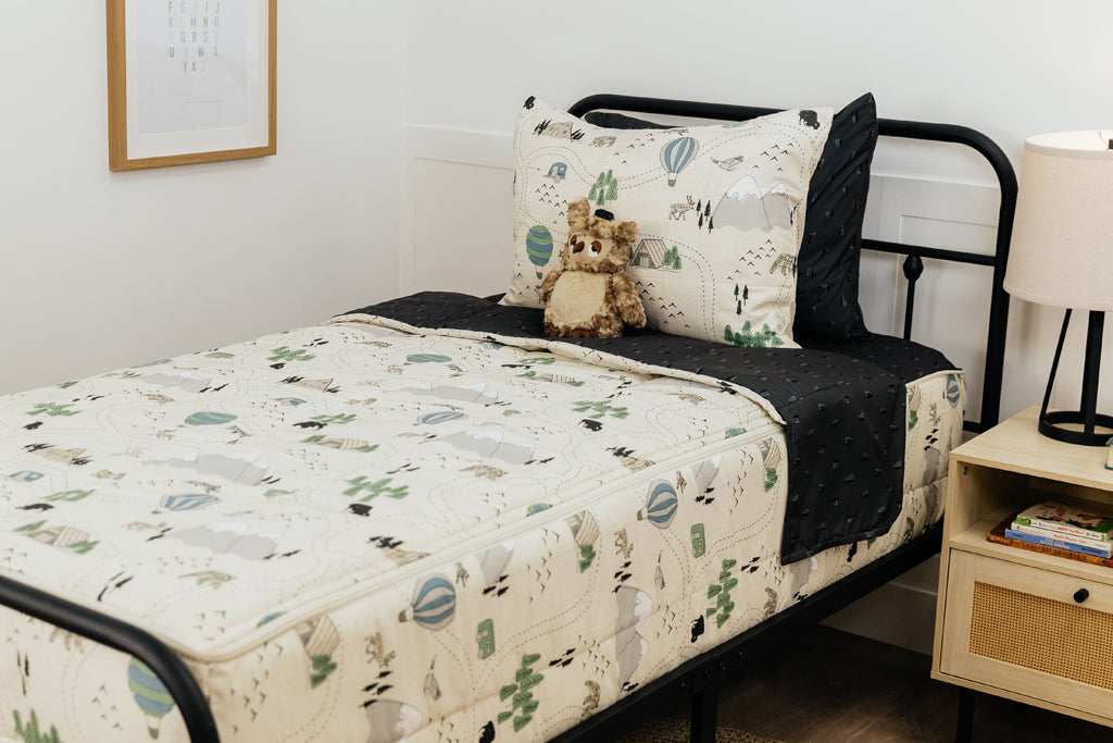 A twin bed made with outdoor themed zipper bedding, a stuffed owl propped up against the pillows.