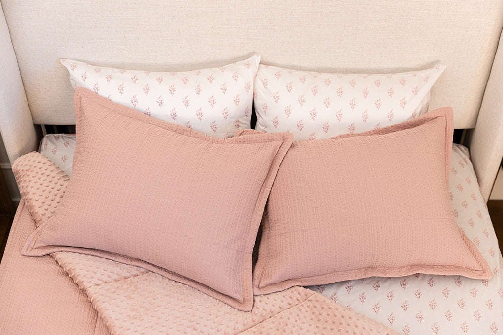 A bed made with woven pink zipper bedding with the comforter pulled back and pillows on top of the bed.