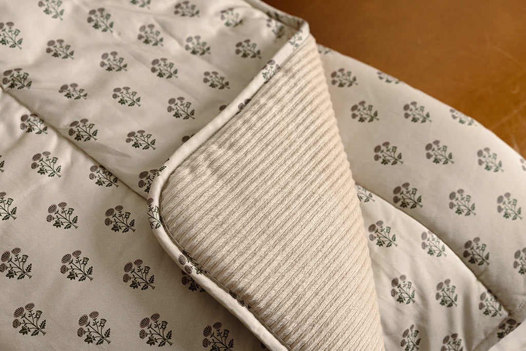 A tan, pink, and green blockprint floral  with cream corduroy minky blanket on an orange leather couch.