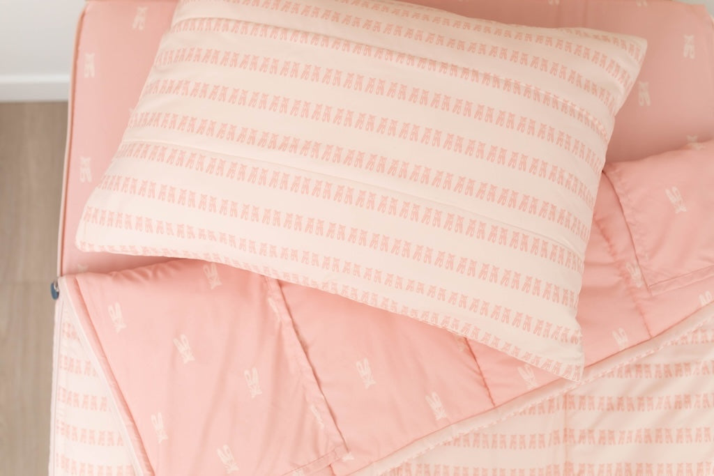 A twin bed made with pink ballet shoes kids zipper bedding, the top unzipped and slightly pulled back and a pillow on the bed.