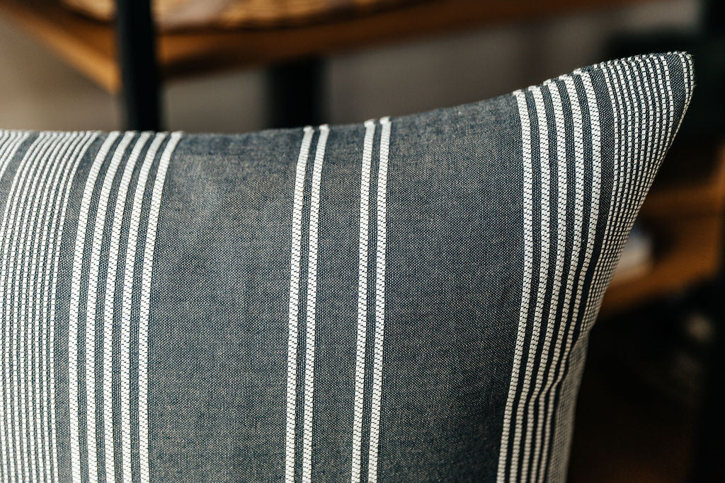 A close up corner view of a woven dark gray and white striped euro pillow.