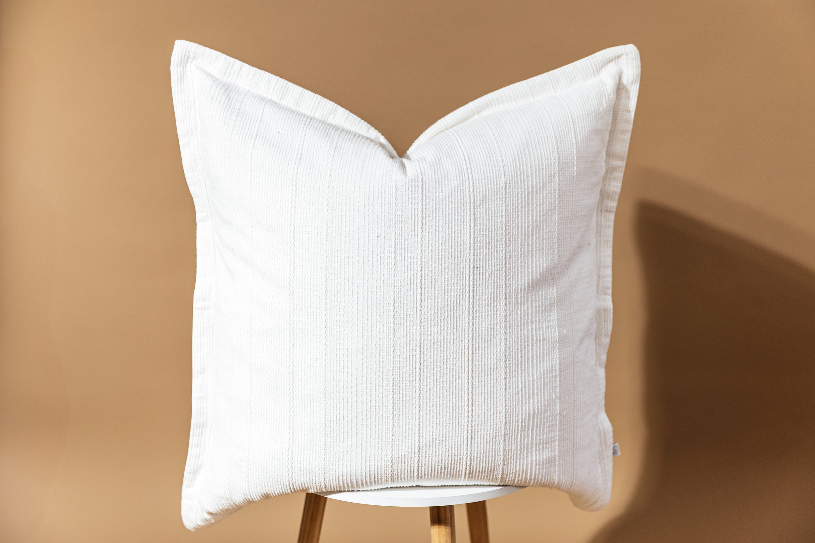 A big white textured pillow arranged on a stool with a brown background behind it.