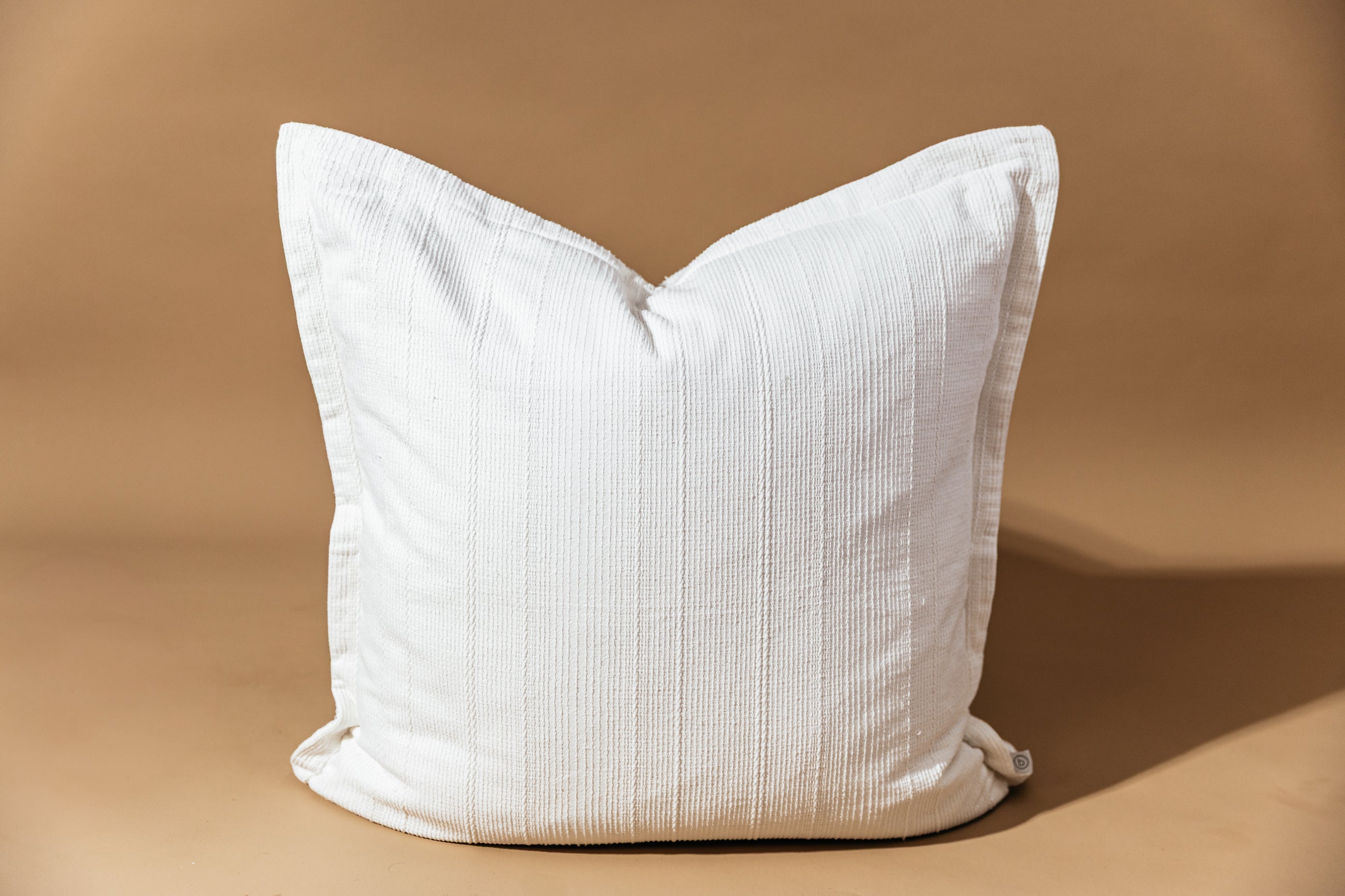 A big white textured pillow on a brown background.