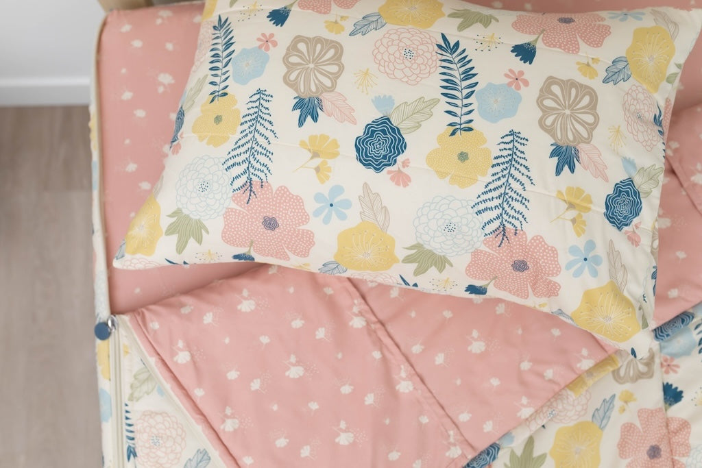 A twin bed made with yellow, pink, and blue floral kids zipper bedding, the top unzipped and slightly pulled back and a pillow on the bed.