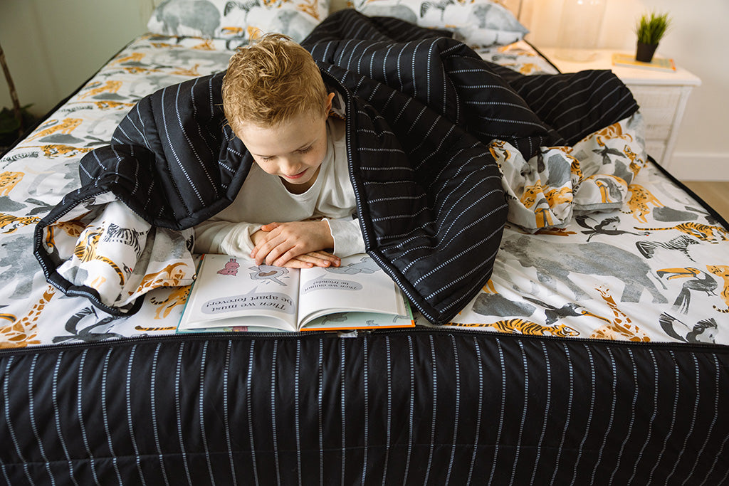 A young boy laying on jungle zipper bedding and reading. 