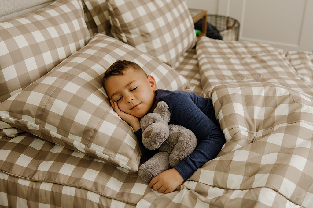 A young boy sleeping in tan gingham print bedding.