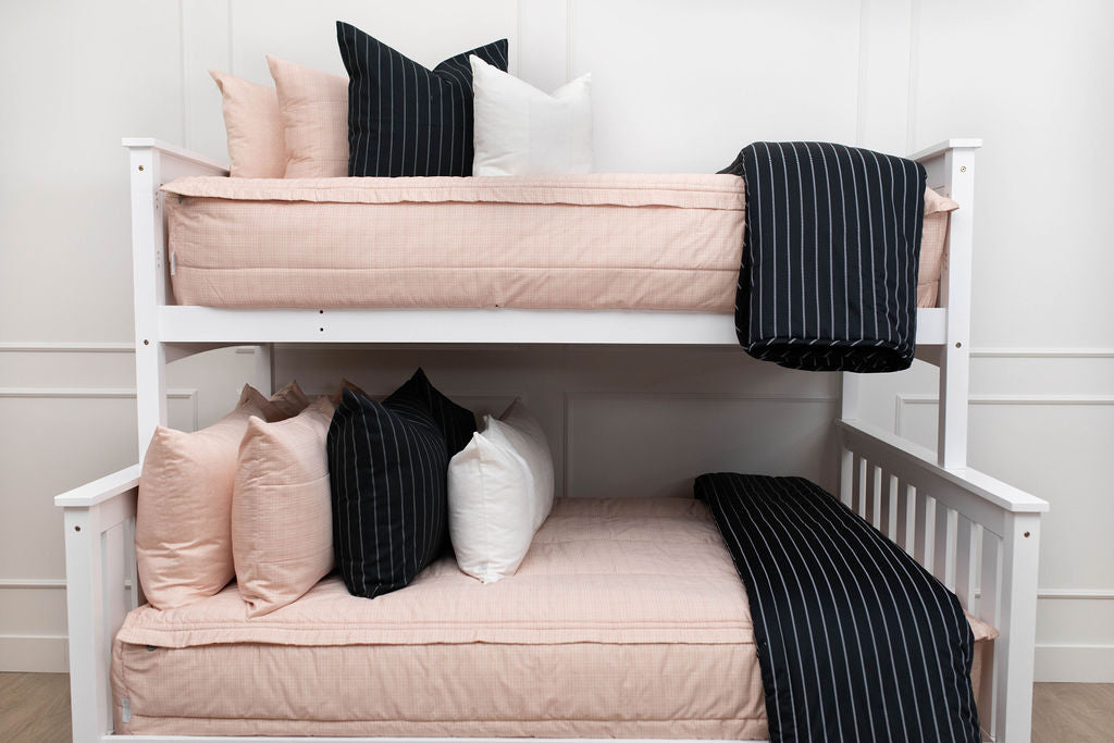 A standard bunk bed with both bunks made with light pink zipper bedding and black and white pillows and blankets.