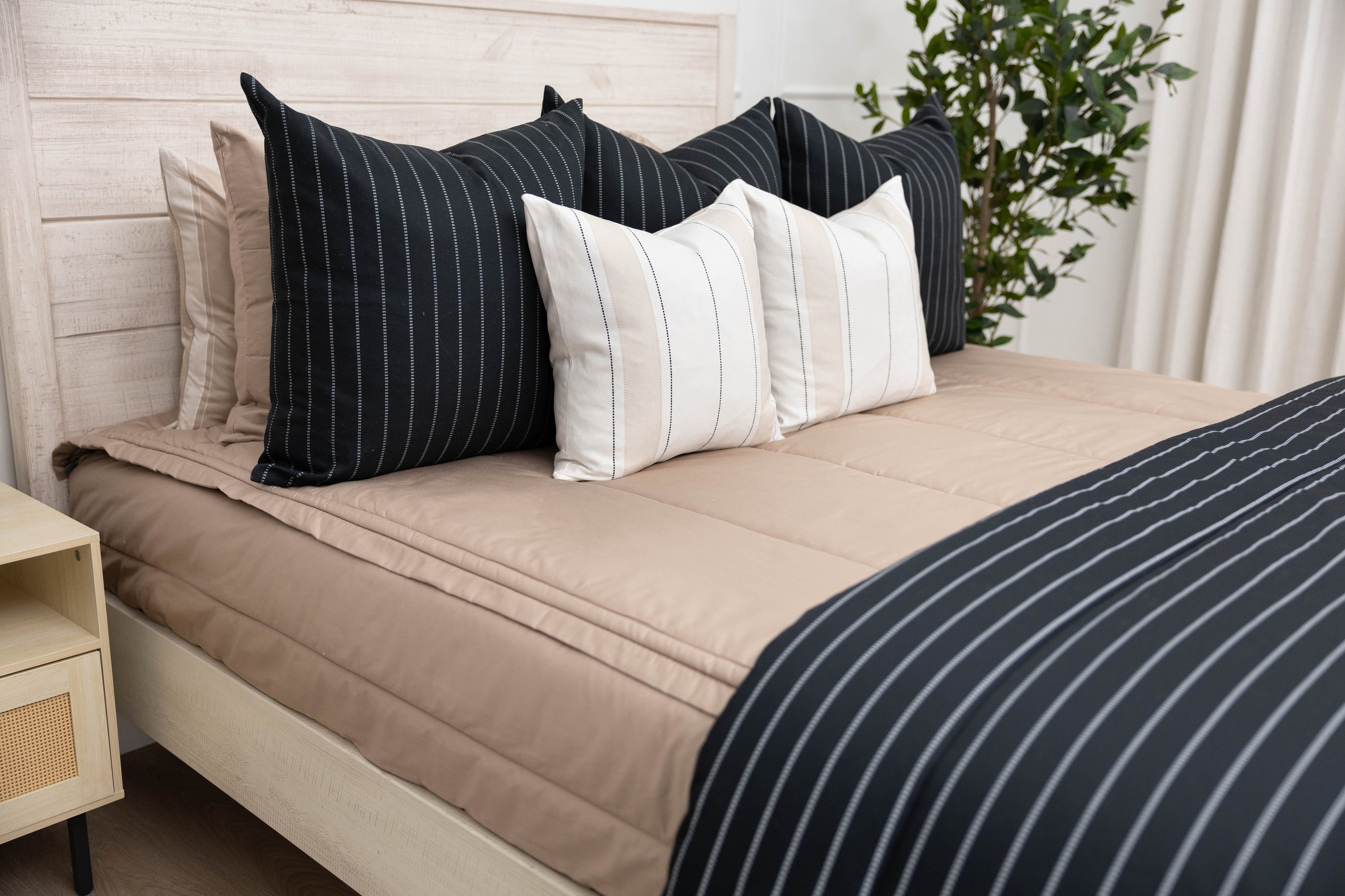 A bed made with tan zipper bedding and an assortment of black striped pillows and blanket.