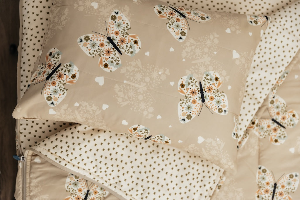 Butterfly printed kids zipper bedding with the top unzipped and one side pulled back to reveal the inside linine, the pillow tossed on top of the bed.