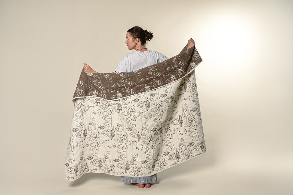 A model holding a cream and brown quilted holiday blanket on a paper backdrop.