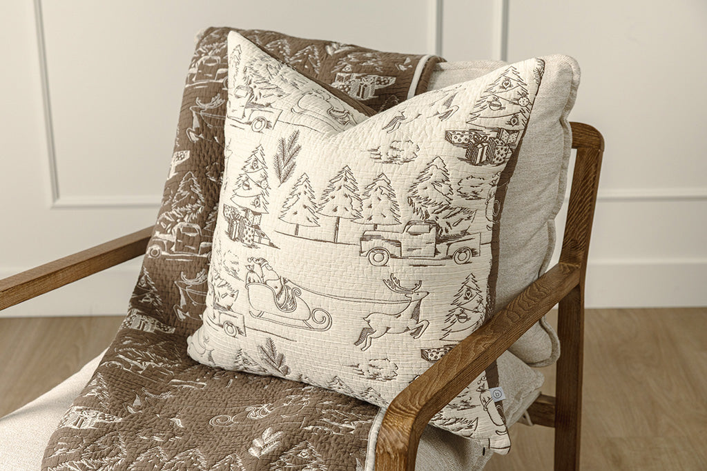 Brown and cream quilted holiday themed pillow and blanket on a chair.