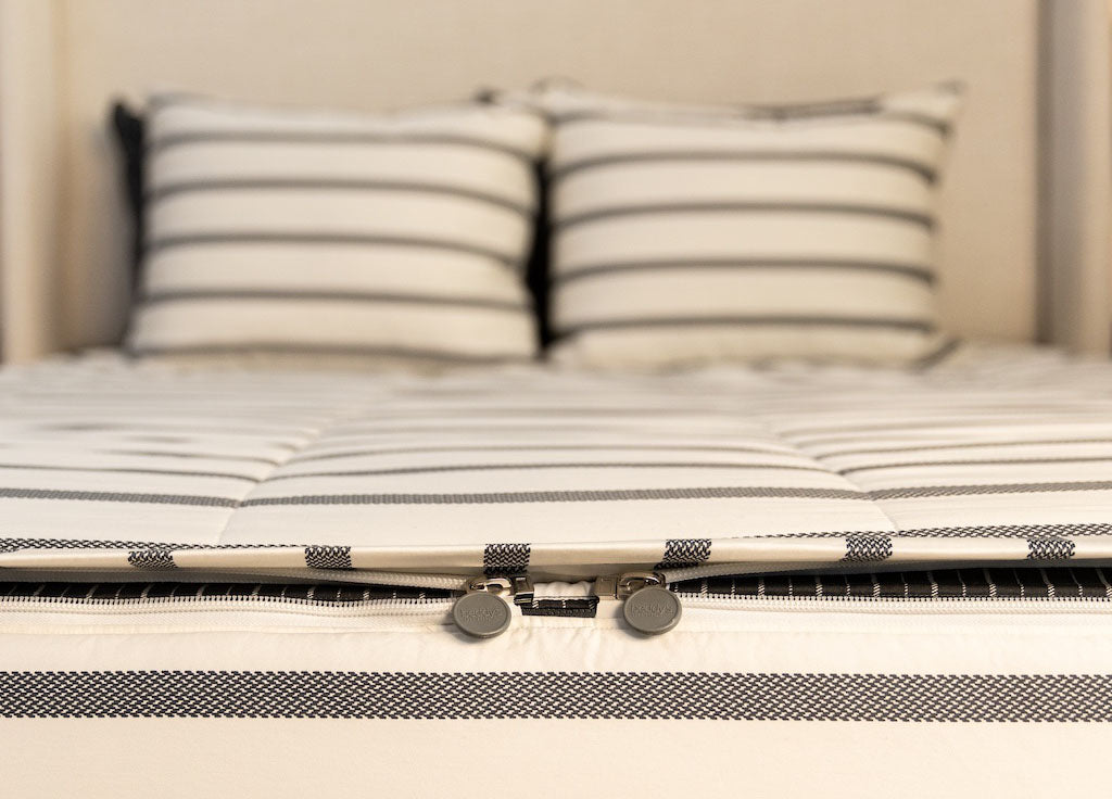 A view of the foot of a bed made with white and black striped zipper bedding with a focus on the two zippers.