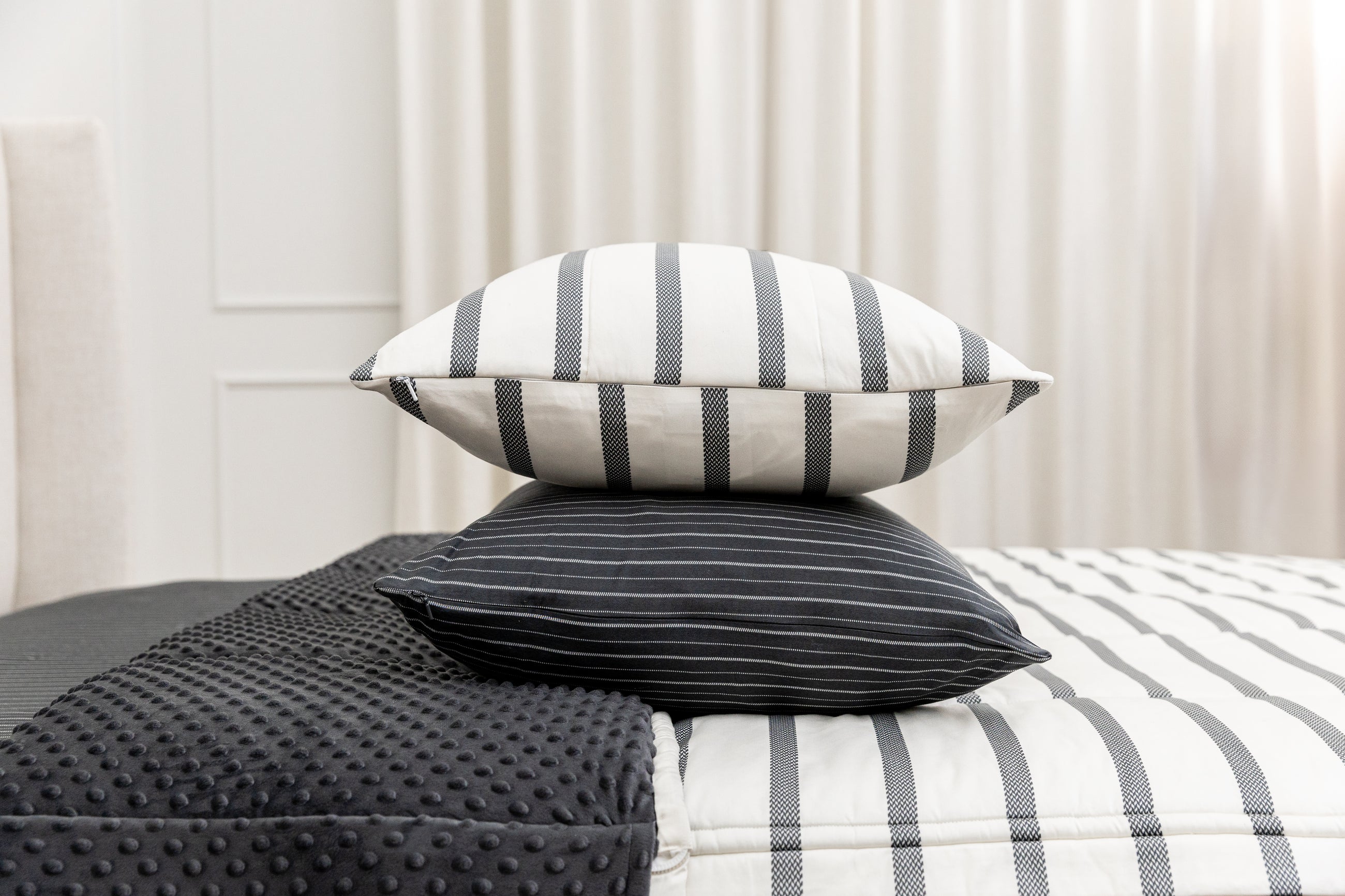 A white striped sham stacked on top of a black striped pillowcase, both sitting on top of a bed made with striped zipper bedding.