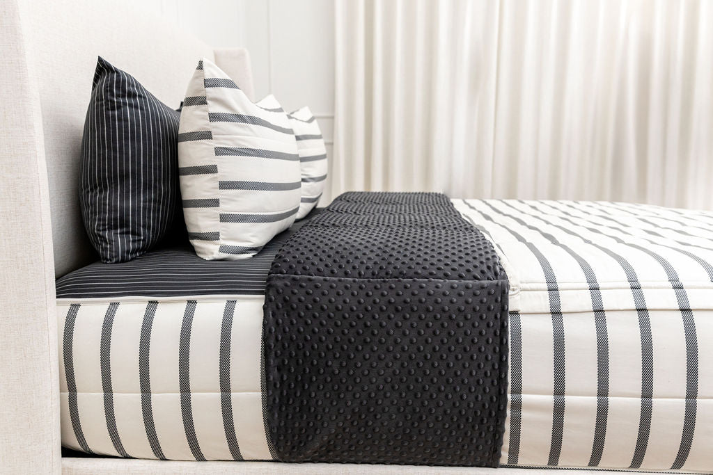 A bed made with striped white and black zipper bedding with the top unzipped and pulled back to show the inside lining.