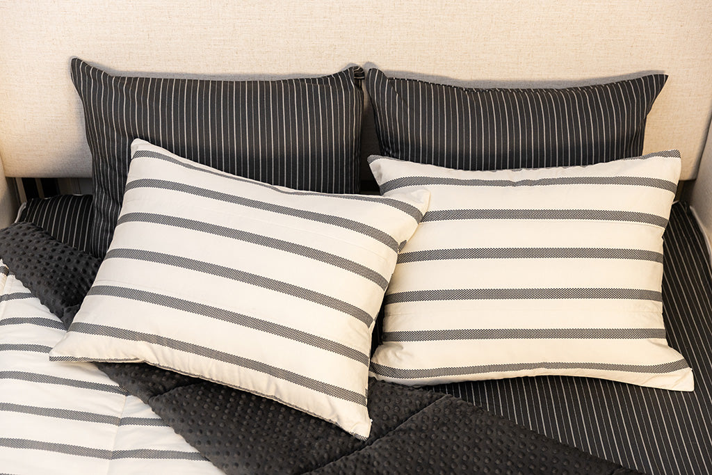 A bed made with white and black striped zipper bedding with the top pulled back to reveal the inside lining, and four pillows arranged on top