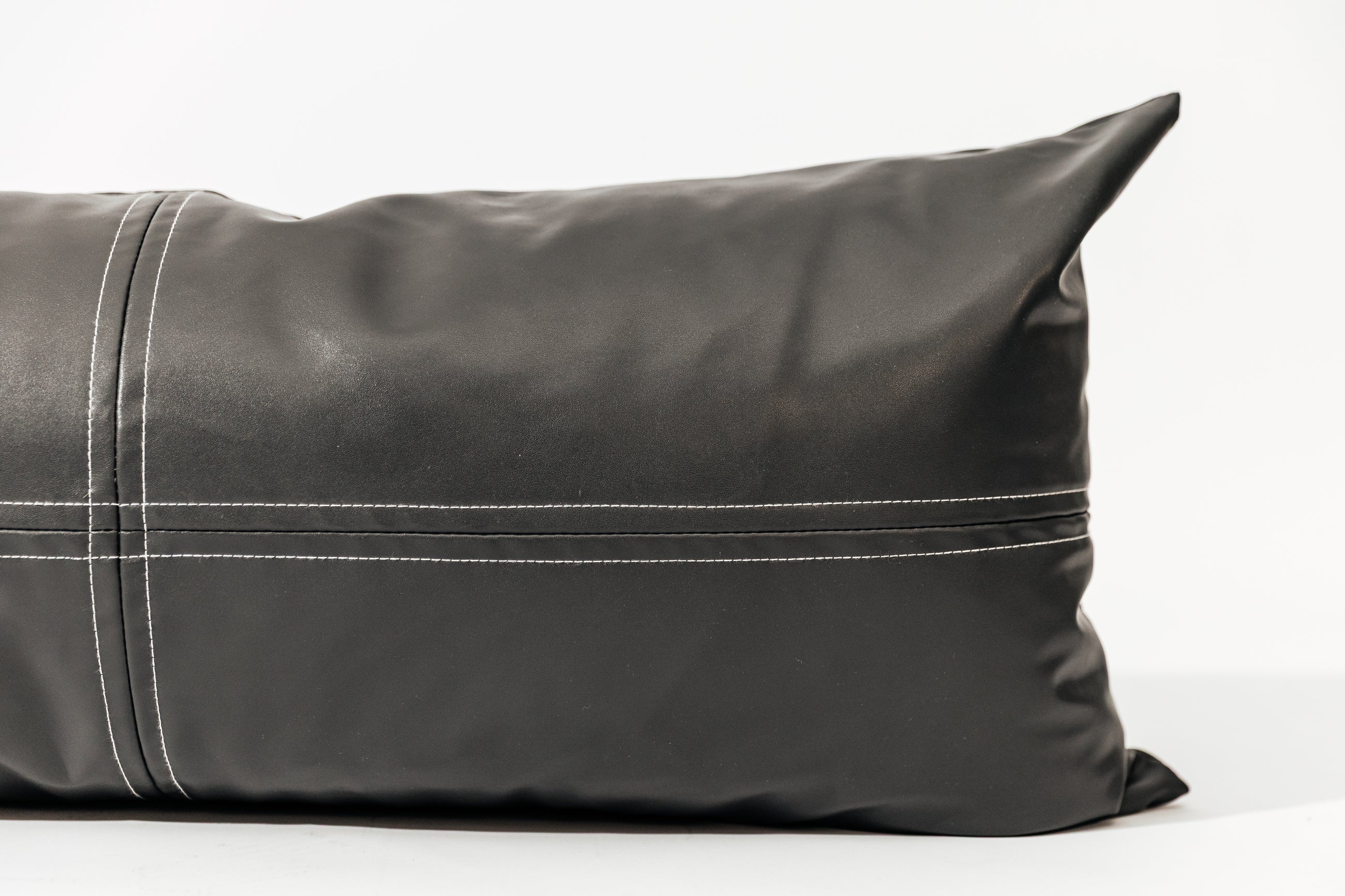 A close up of a charcoal lumbar pillow on a white backdrop.