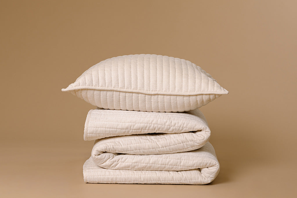 A cream chenille and minky blanket and pillow stacked on a tan paper backdrop.