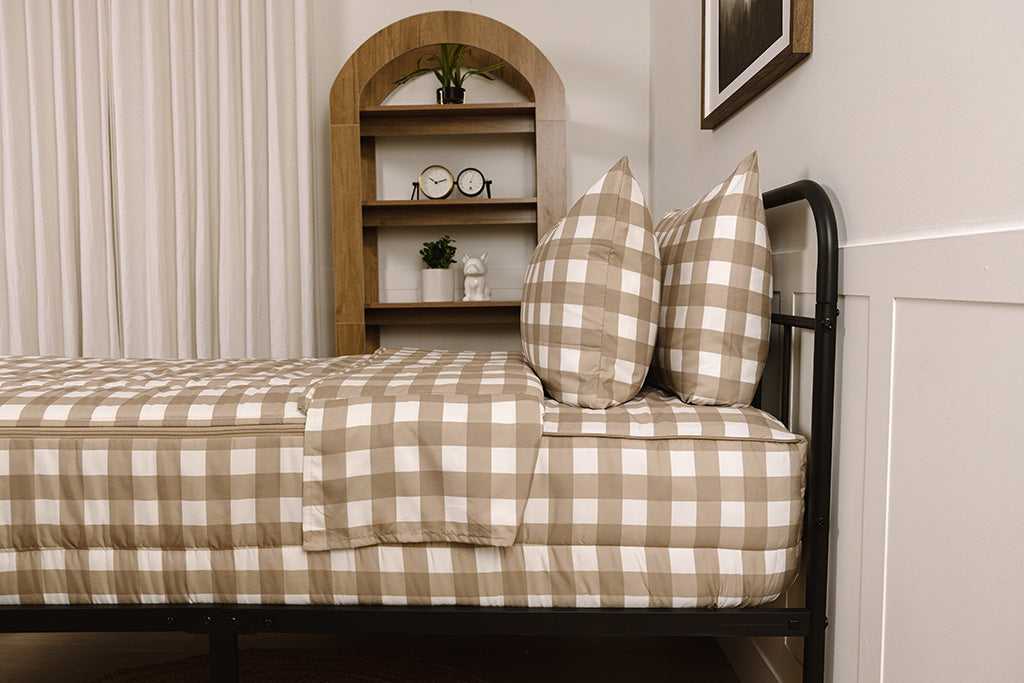 A bed made with tan gingham printed zipper bedding, showcasing the pillowcase and sham and the top of the bedding turned down to show the inside lining. 