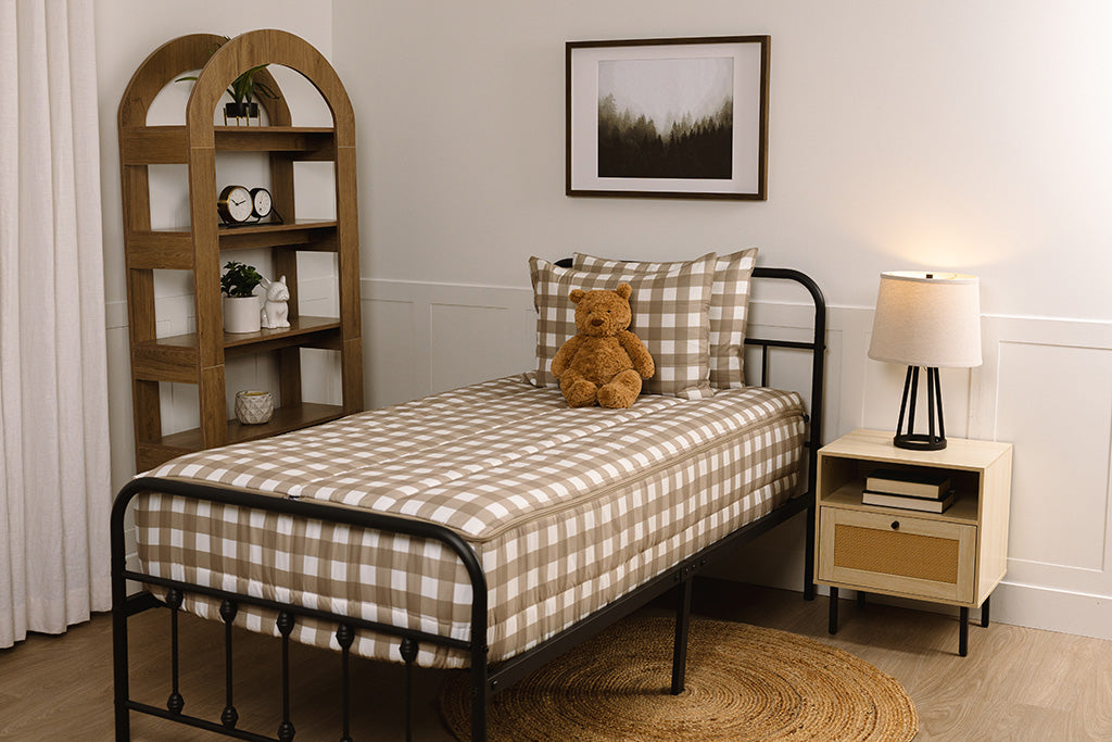 Children's zipper bedding in a bedroom on a black bed frame that has a tan gingham print, with a stuffed toy laying against the pillow.