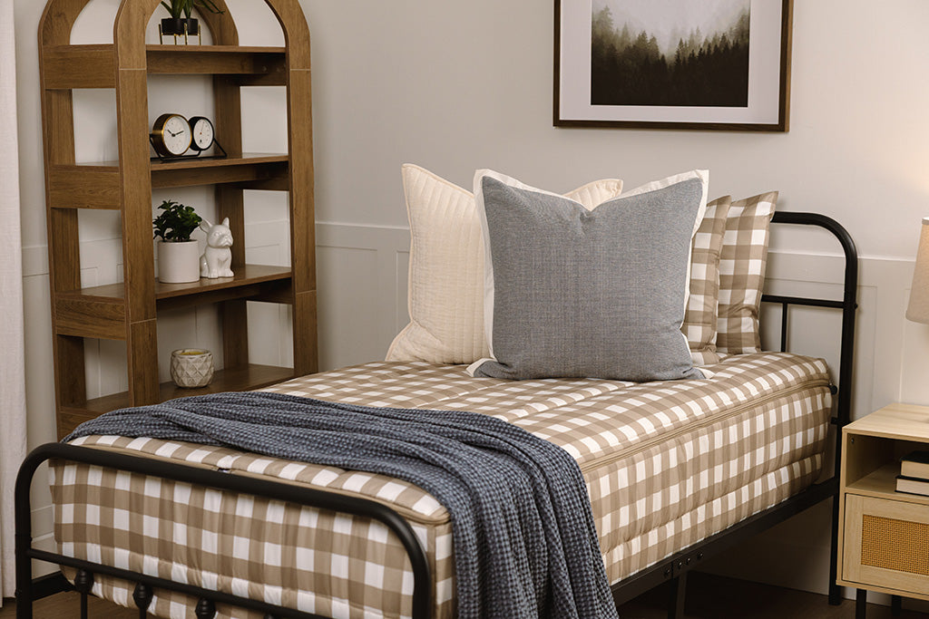 Children zipper bedding in a bedroom on a black bed frame that has a tan gingham print, with cream and blue colored accessories. 