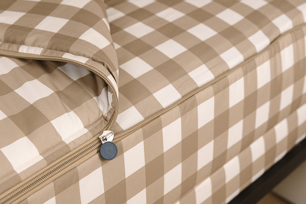 A tight shot of the zipper feature on a set of tan gingham printed zipper bedding.