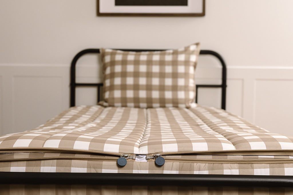A shot of the two zippers on a set of tan gingham zipper bedding, the zippers completely unzipped to show how they meet at the foot of the bed. 