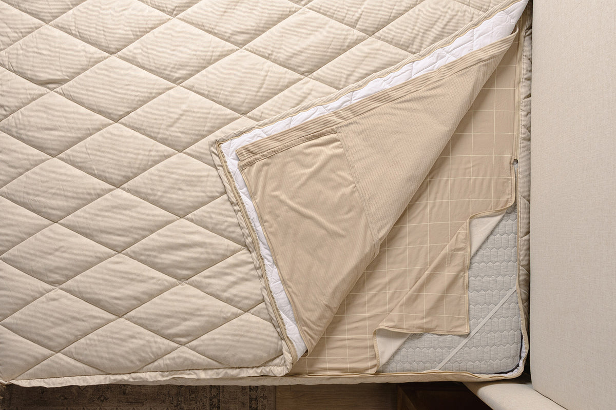 Overhead shot of tan stripe quilted zipper bedding layers.