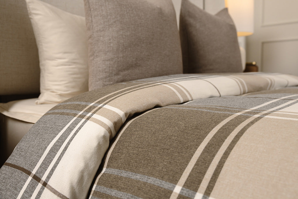 A brown, gray, and white plaid duvet on cream sheets on a bed.