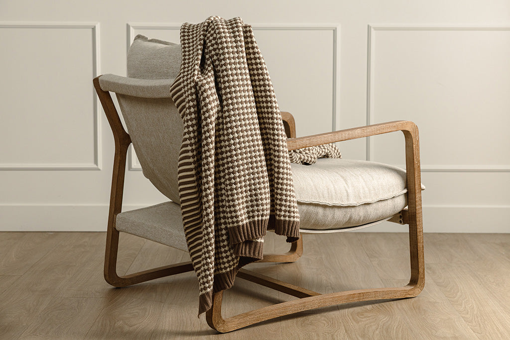 A brown and cream scallop weave throw on a wood and oat colored chair.
