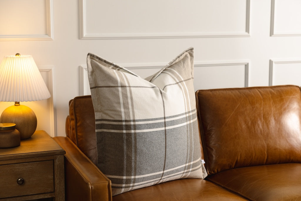 A brown, gray, and white plaid pillow on a leather couch.