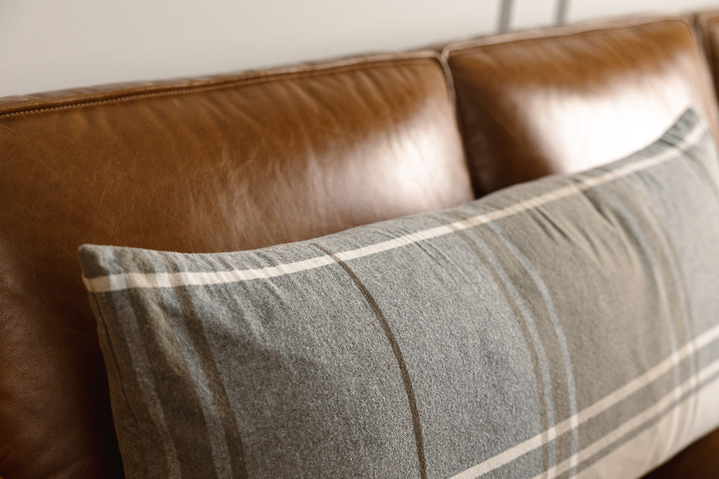 Close-up shot of a brown, gray, and white xl lumbar pillow on a leather couch.