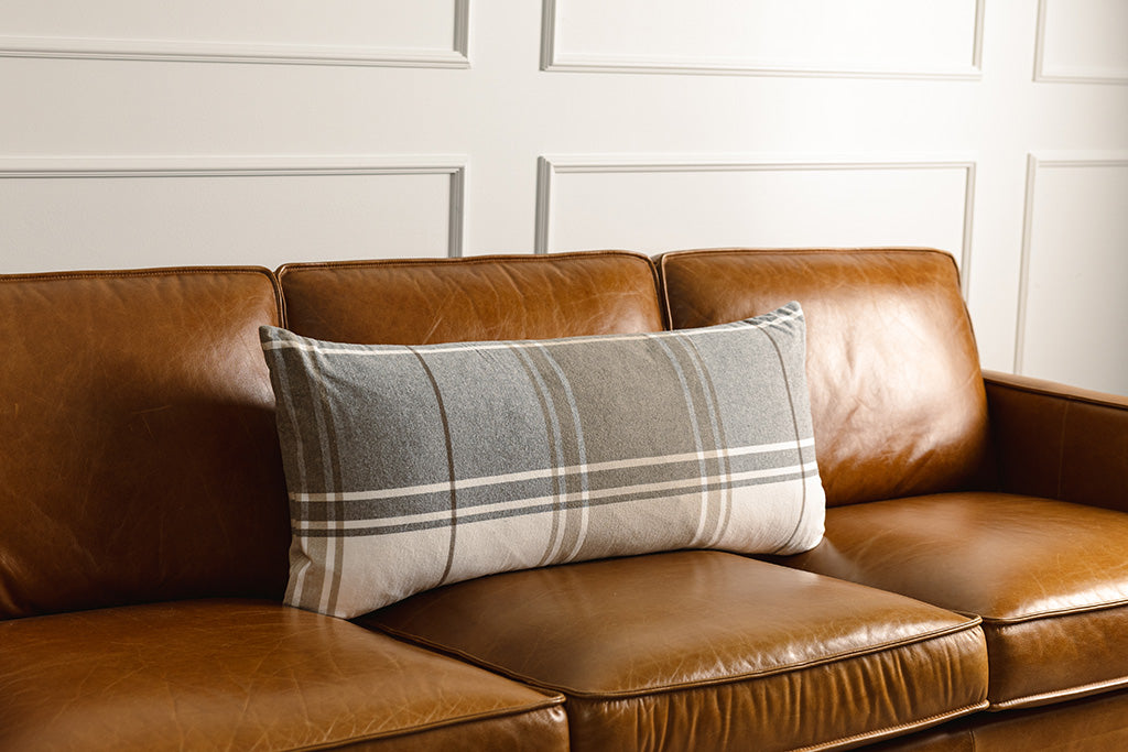 Brown, gray, and white xl lumbar pillow on a leather couch.