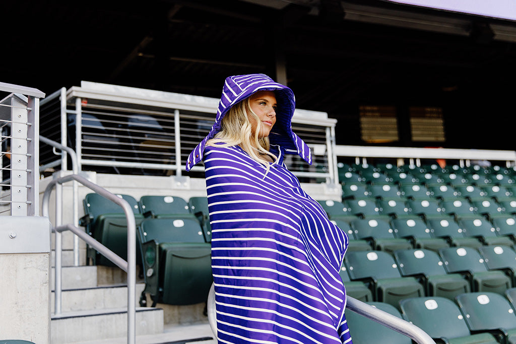 A woman standing in a baseball stadium wrapped in a purple and white striped blanket.