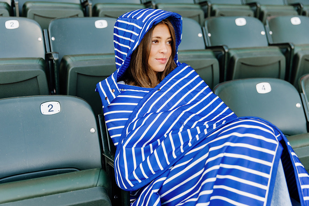 A woman sitting in a baseball stadium wrapped in a blue and white striped blanket.