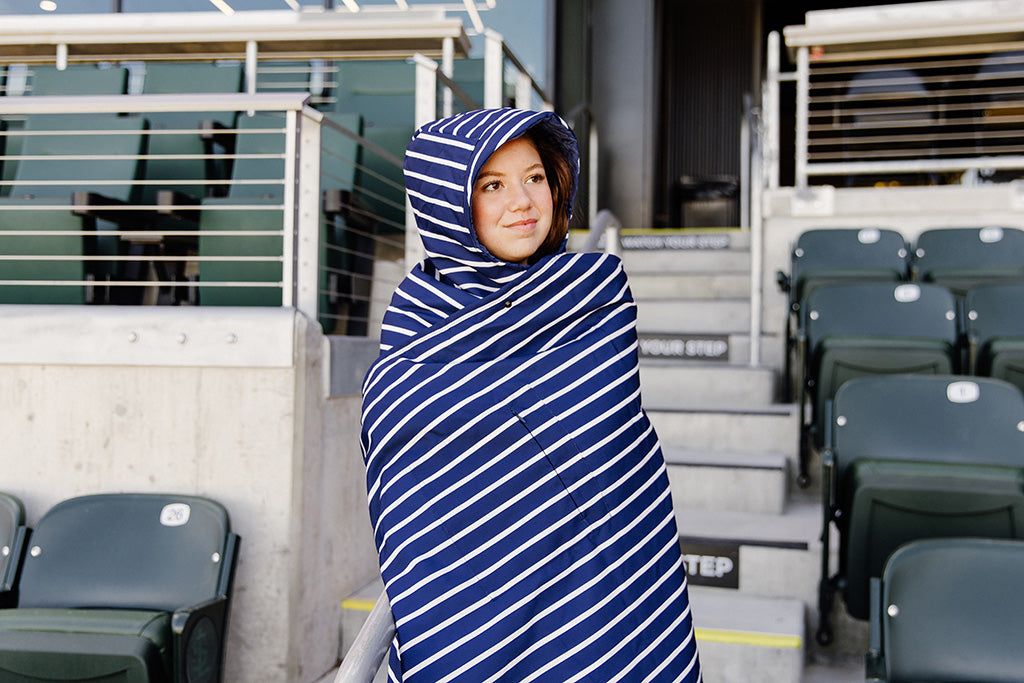 A woman standing in a baseball stadium wrapped in a navy  and white striped blanket.